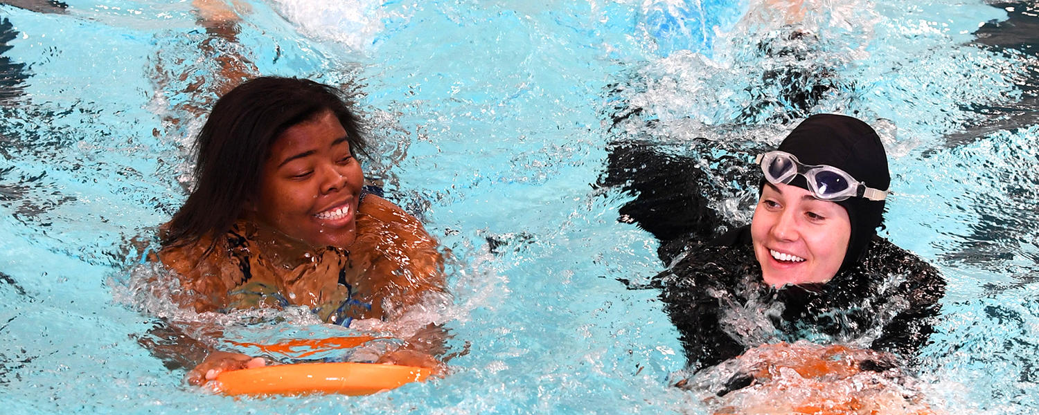 Two women swimming laps with flutter boards