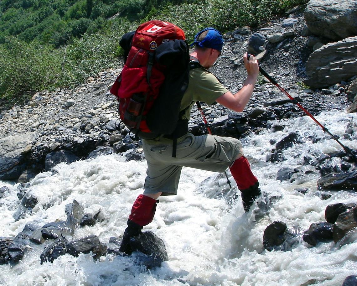 Man hiking across rocks in water using poles